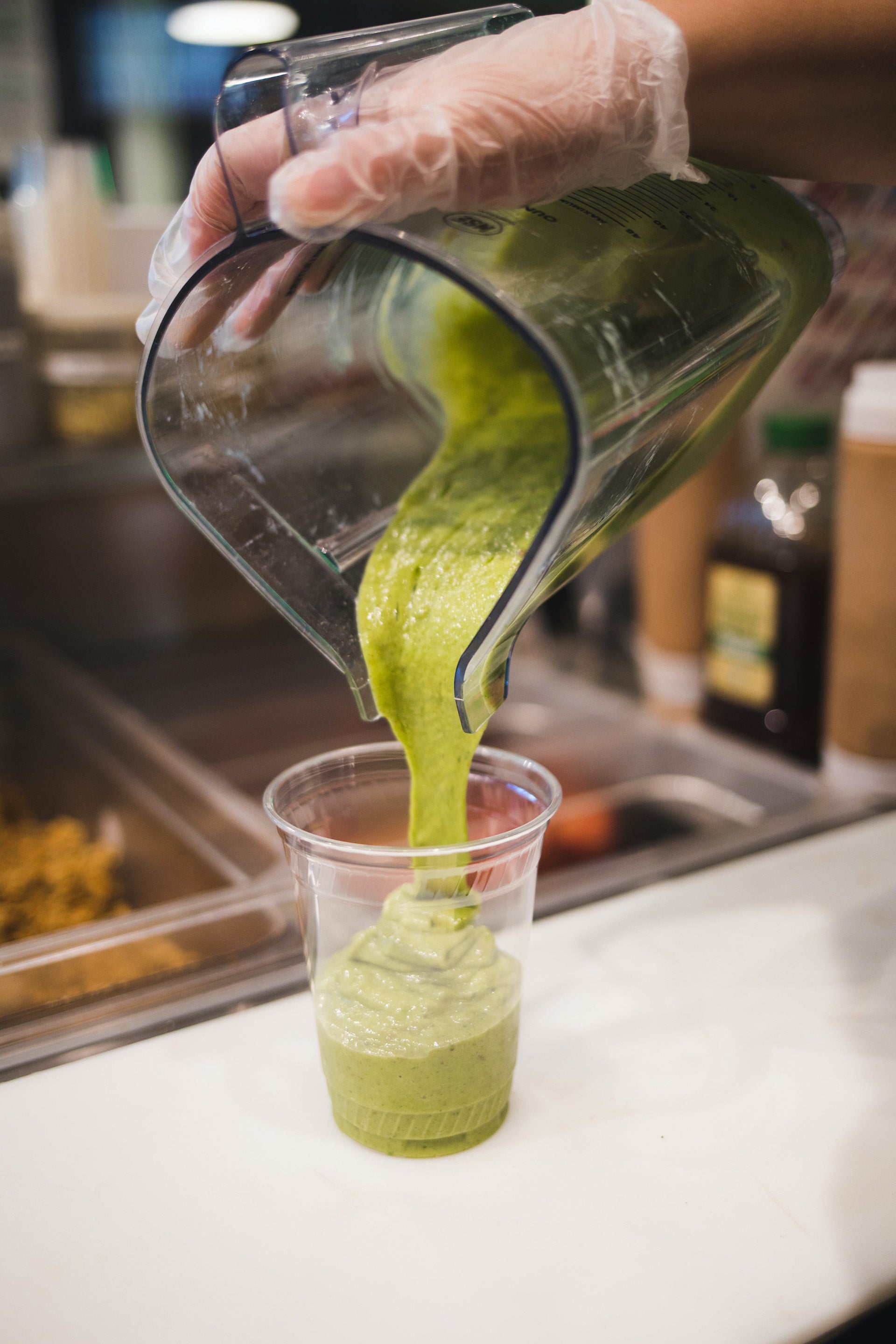 A green smoothie being poured into a cup at a smoothie shop.